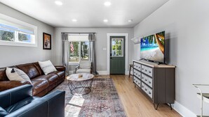 A living room with a brown leather sofa, a coffee table, a TV on a stand, and a patterned rug. - Experience Cheyenne in a cozy home, close to Downtown, Medical Center and CFD.  (Cheyenne)