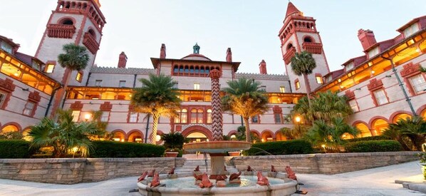 A large, historic building with multiple towers and arched windows, surrounded by palm trees and a central fountain.