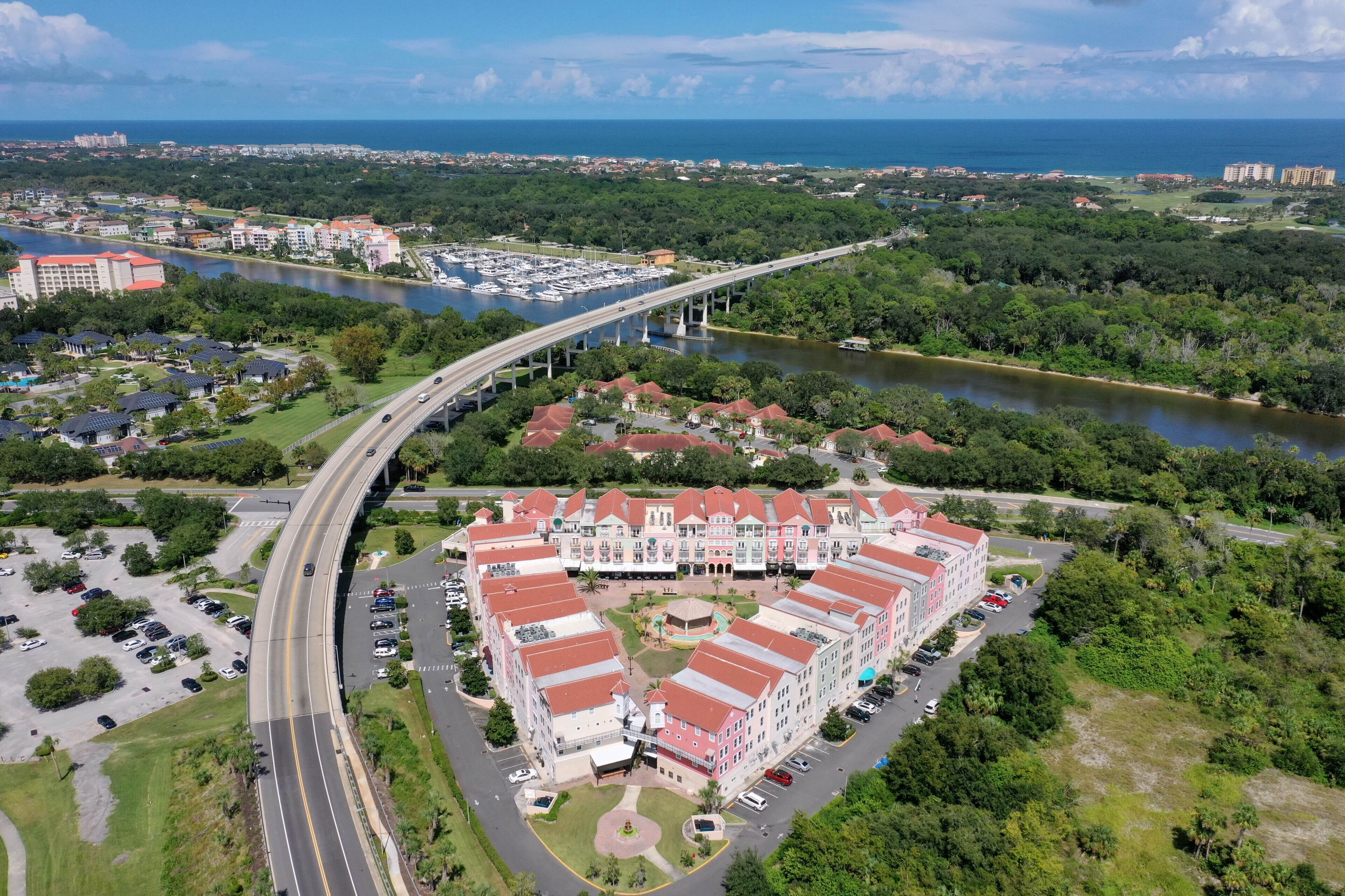 An aerial view of a hotel with a central courtyard, surrounded by lush greenery and a river. A bridge spans the river, connecting different parts of the property.