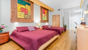 Habitación de hotel con dos camas, suelo de madera, cómoda de madera, escritorio y espejo.