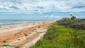 Una playa con orilla arenosa, una zona cubierta de césped y una torre de agua al fondo.