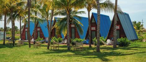A row of blue-roofed cabins with palm trees in front, surrounded by a grassy area.