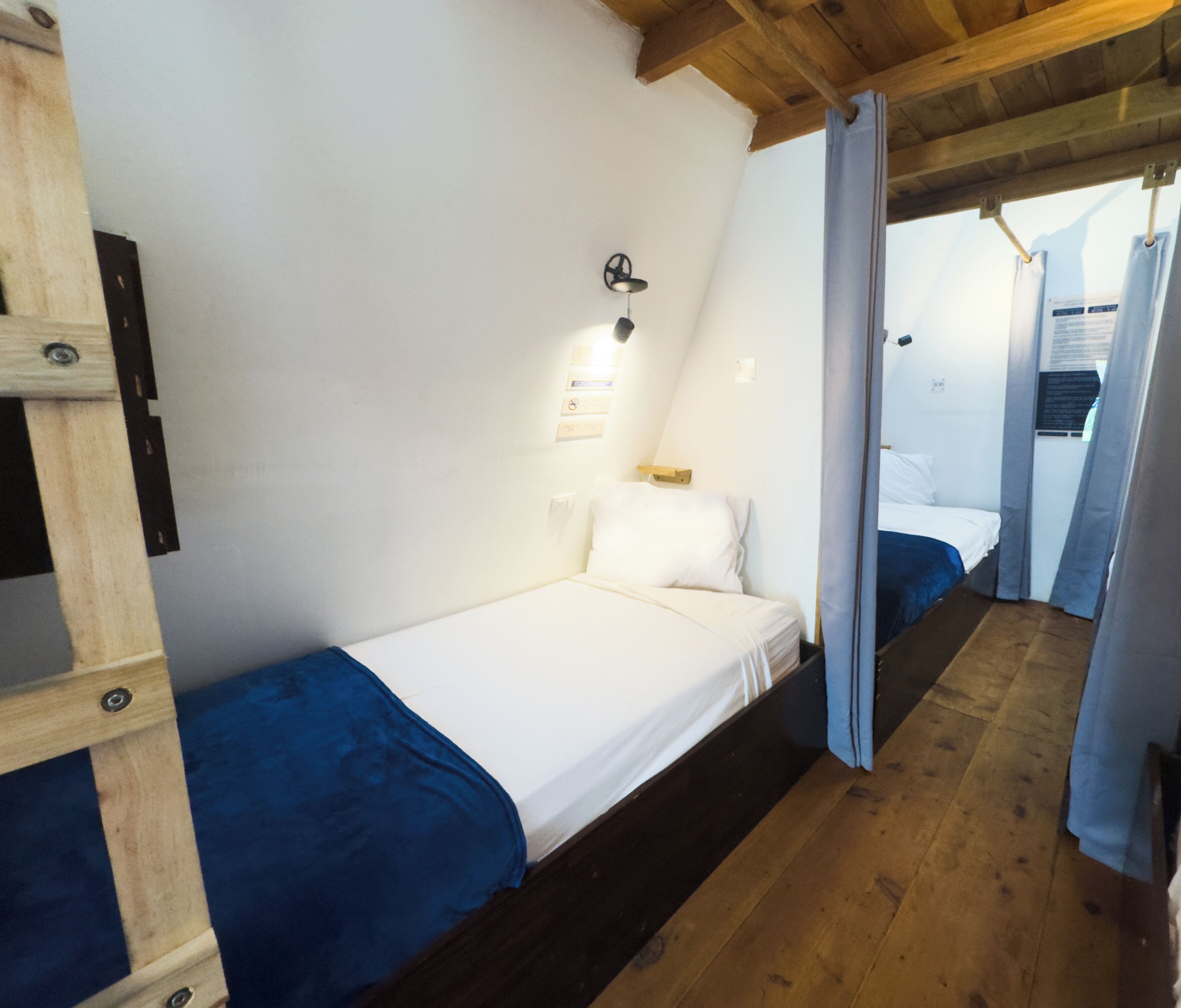 Una habitación pequeña con una cama individual, techo de madera y una cama sencilla con colchón blanco y ropa de cama azul.