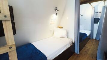 Una habitación pequeña con una cama individual, techo de madera y una cama sencilla con colchón blanco y ropa de cama azul.