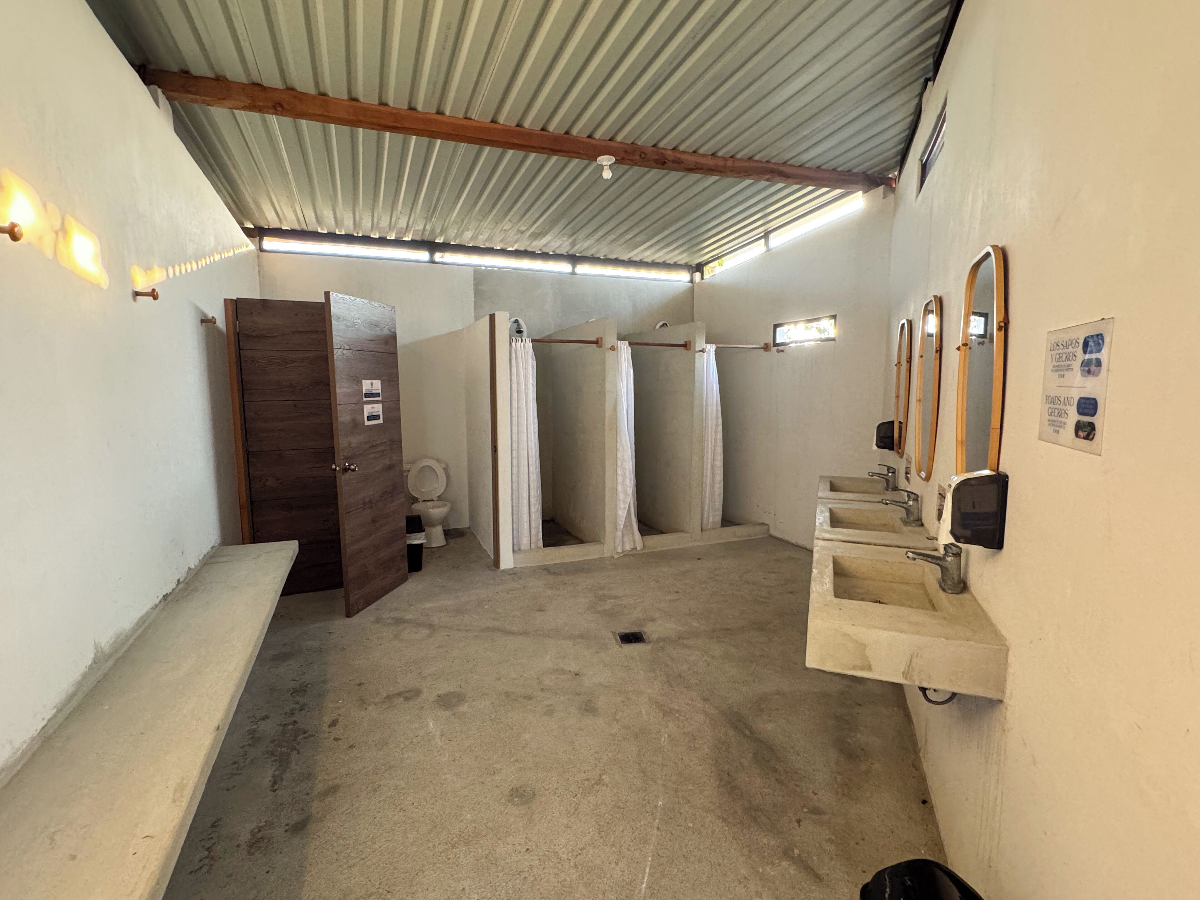 A restroom with a wooden door, three stalls, a sink, and a mirror.