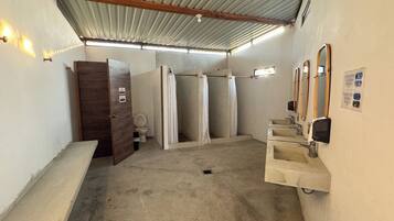 A restroom with a wooden door, three stalls, a sink, and a mirror.