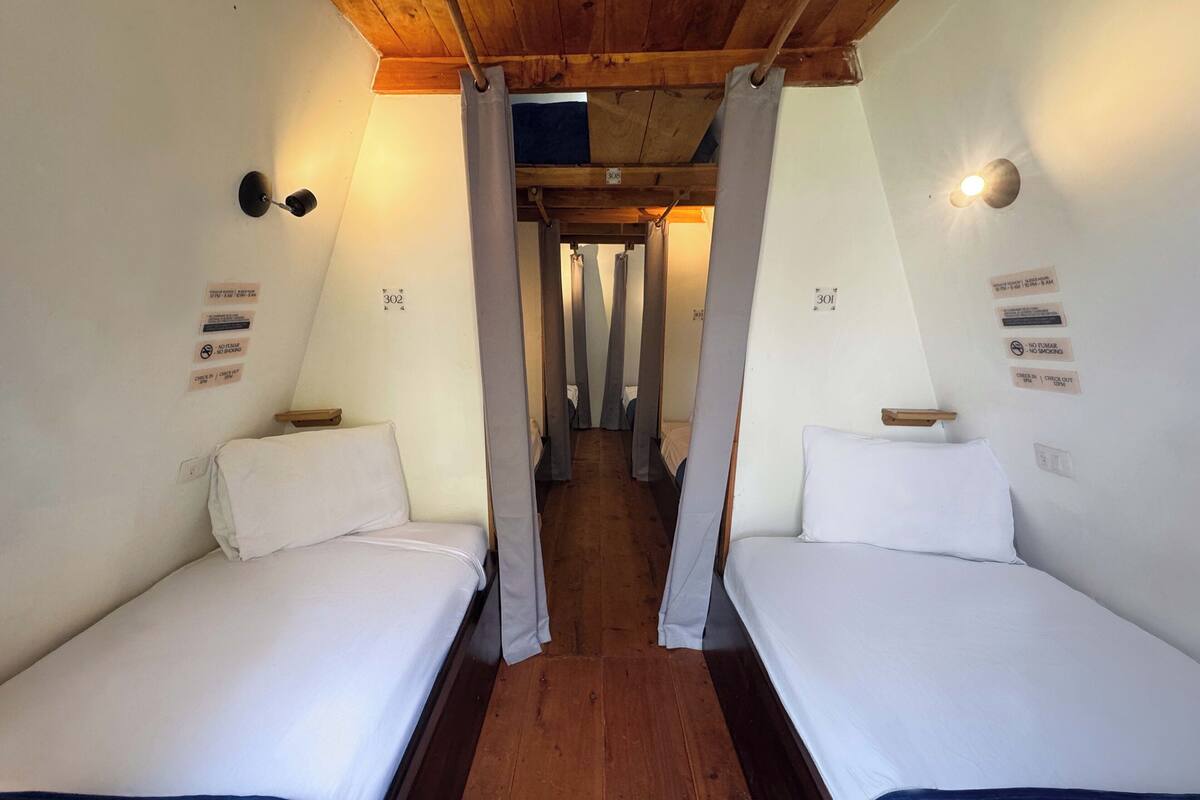Ein Zimmer mit zwei Betten, Holzboden und Holzziel. An den Wänden befinden sich Schilder mit Zimmernummern und Regeln.