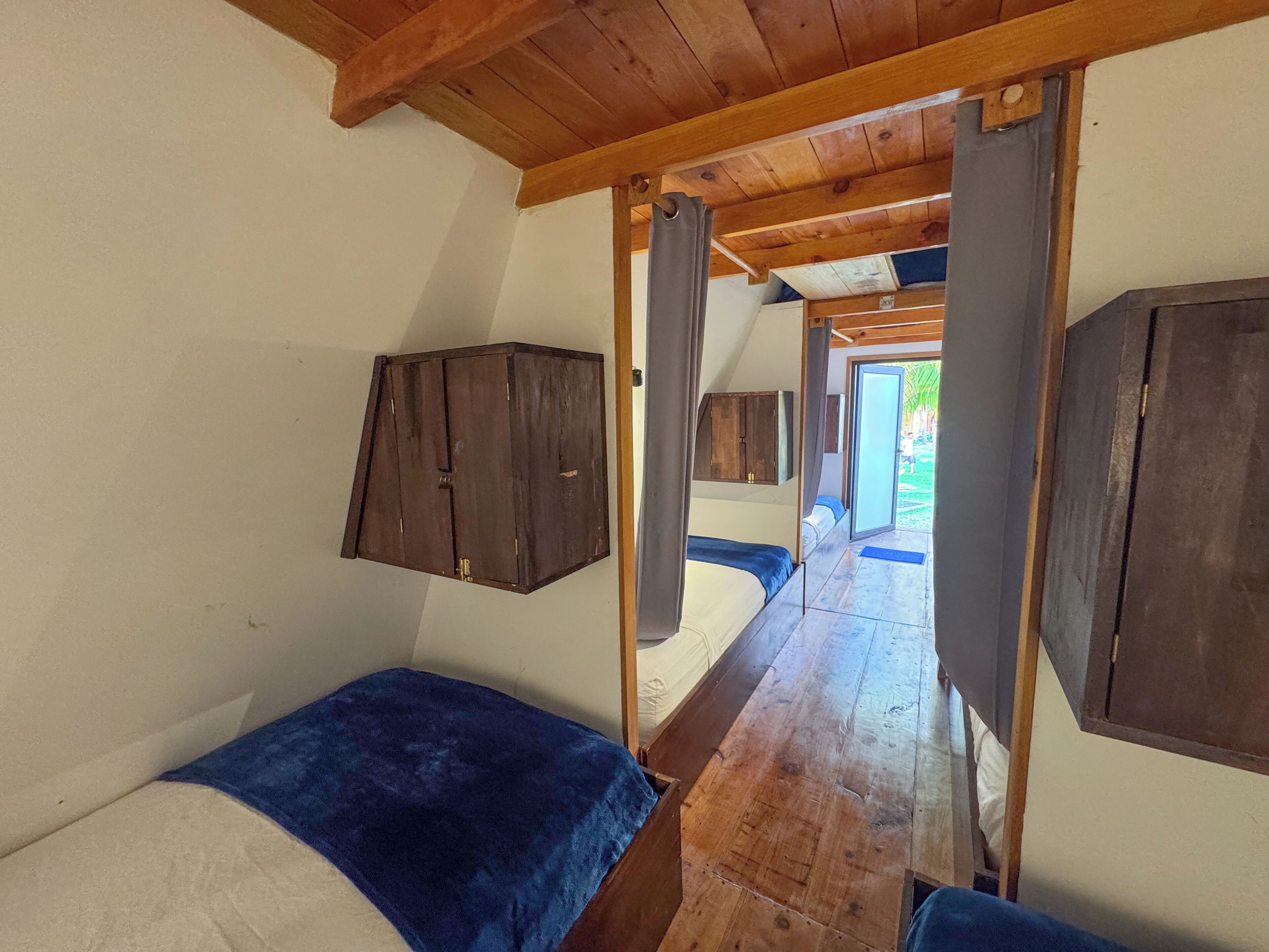 A compact room with a wooden ceiling, a bed with a blue blanket, and a wooden cabinet.