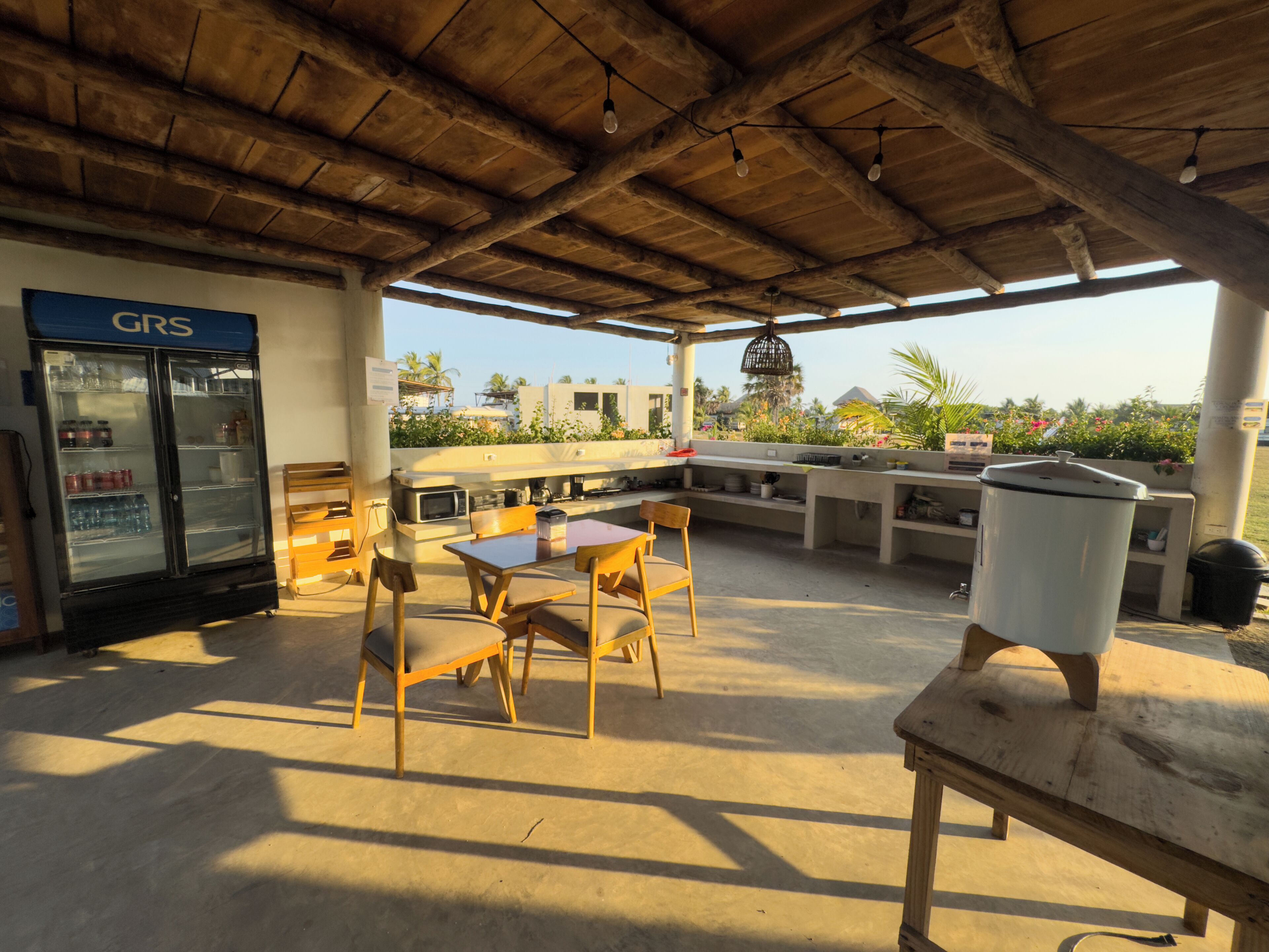 An outdoor patio area with a concrete floor, wooden furniture, a refrigerator, and a large white container.