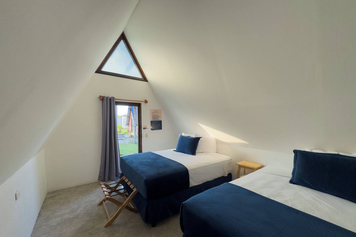 Ein kleiner, dreieckiger Raum mit zwei Betten, einem Holzstuhl und einem Fenster.