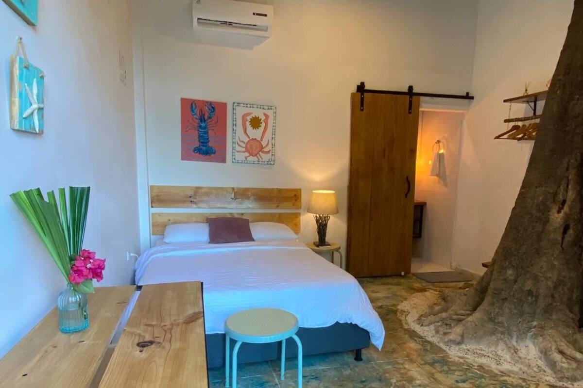Une chambre à coucher avec un lit, une table de chevet, une lampe et un grand tronc d’arbre dans un coin.