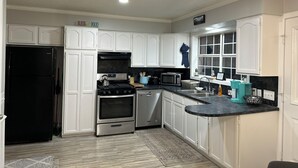 Una cocina con gabinetes blancos, un refrigerador negro, una estufa, un microondas y un lavamanos.