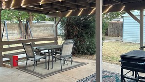 Un patio techado con mesa, sillas, una parrilla y luces colgantes.