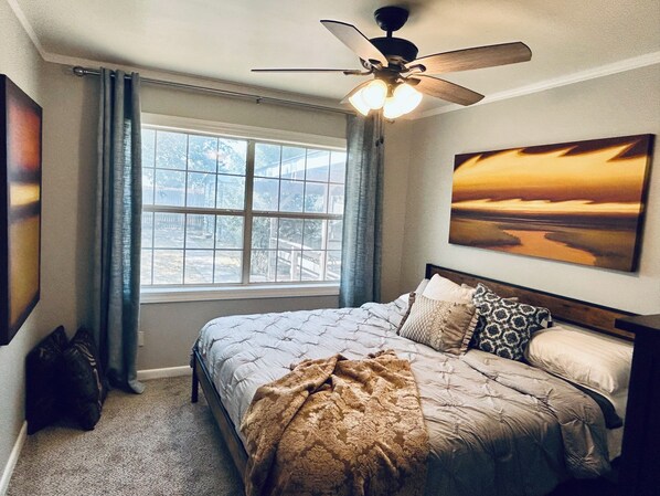 A bedroom with a bed, a ceiling fan, a window with curtains, and a painting on the wall.