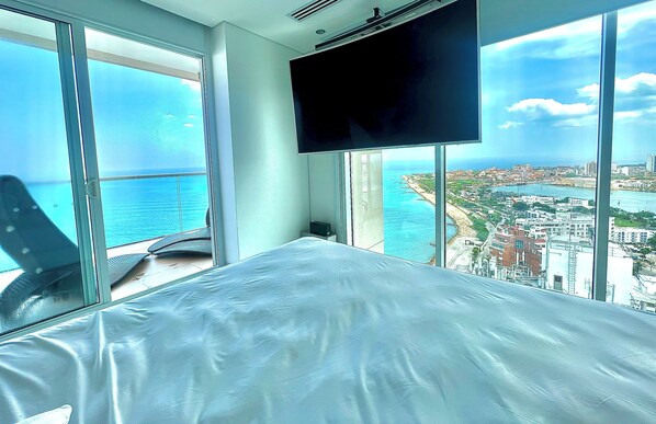 Habitación de hotel con una cama grande, televisión y vistas a la ciudad y al mar.
