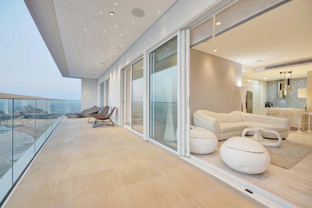 A modern interior with a glass balcony, a sofa set, and a kitchen area.