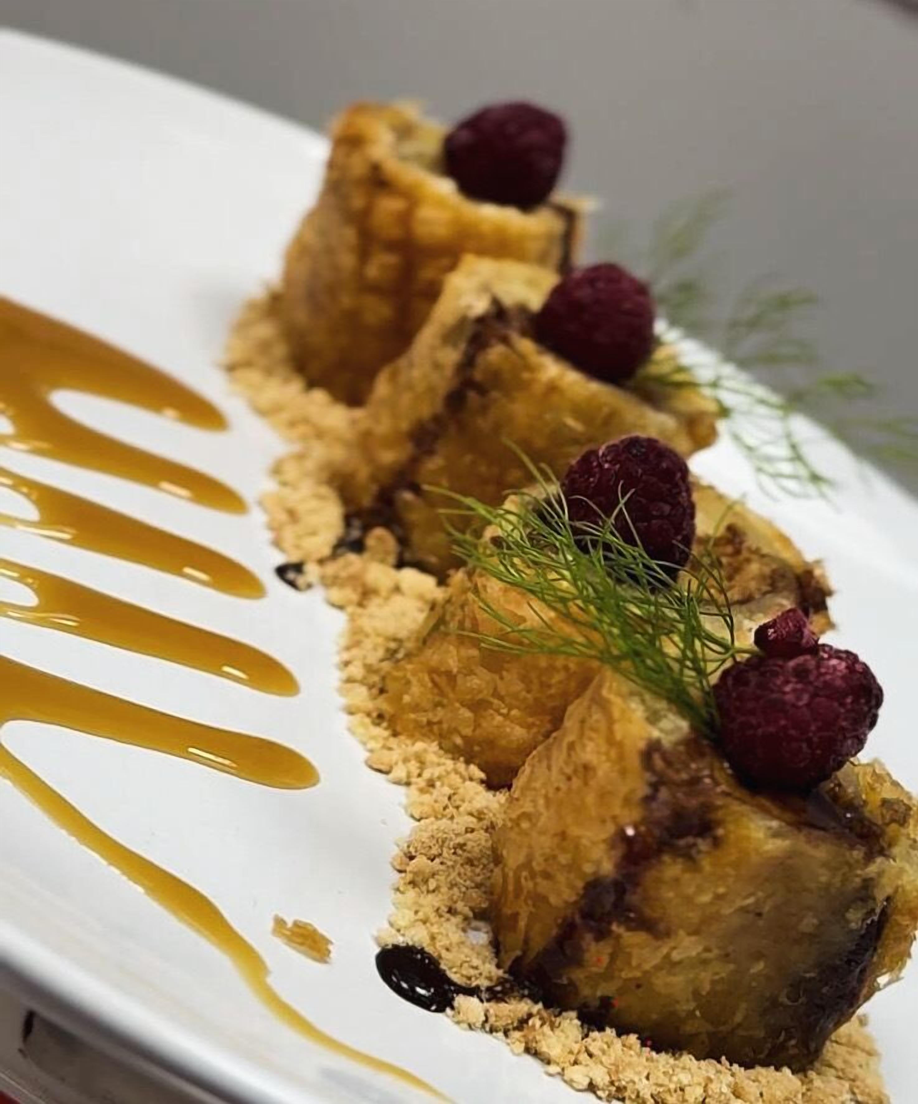 A dessert with a golden drizzle, raspberry, and a sprig of dill on a white plate.