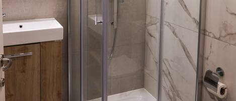 A modern bathroom with a glass-enclosed shower, a wooden vanity, and a patterned floor.