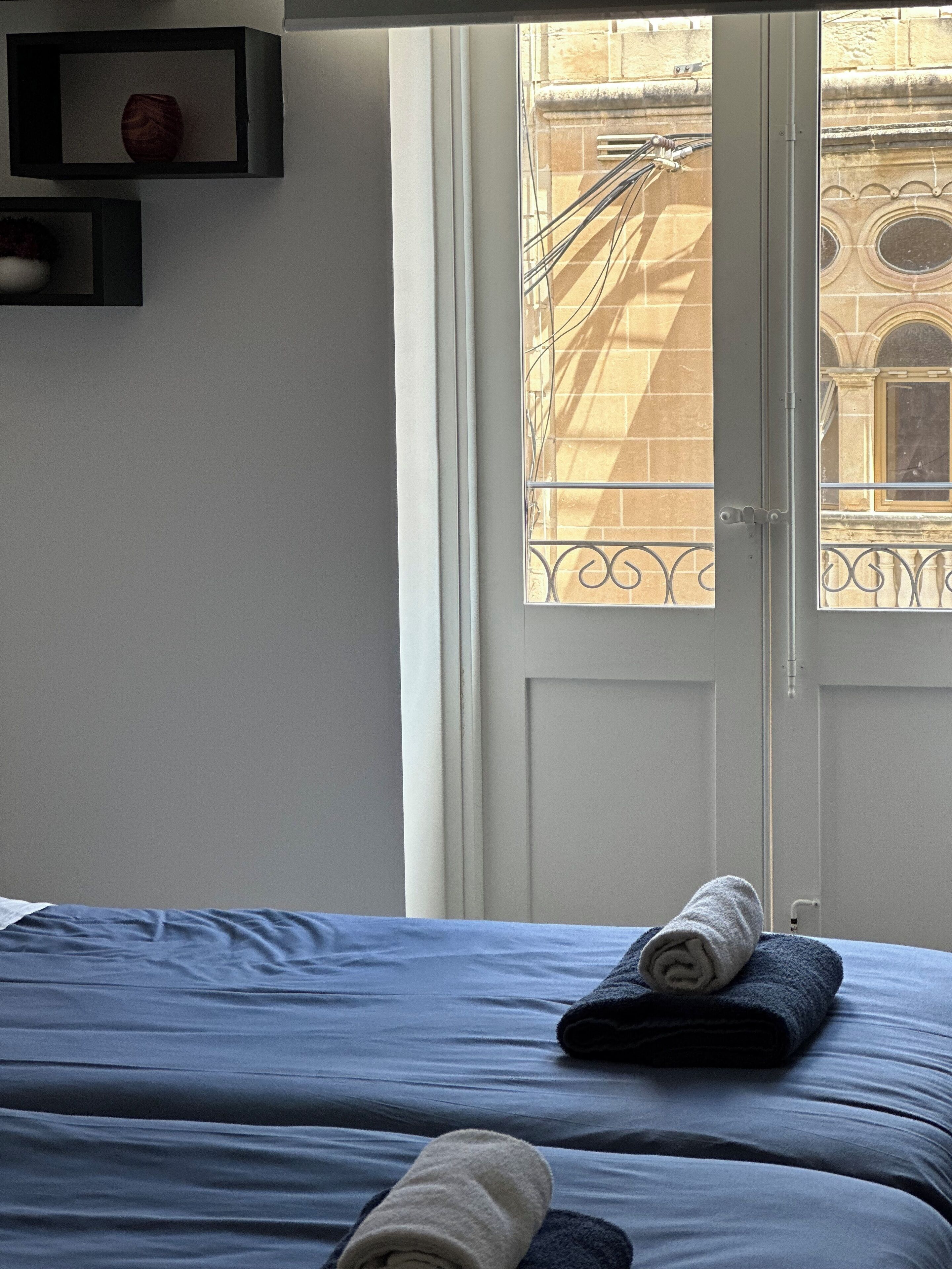 A hotel room with a bed, a door, and a view of a building with a balcony.