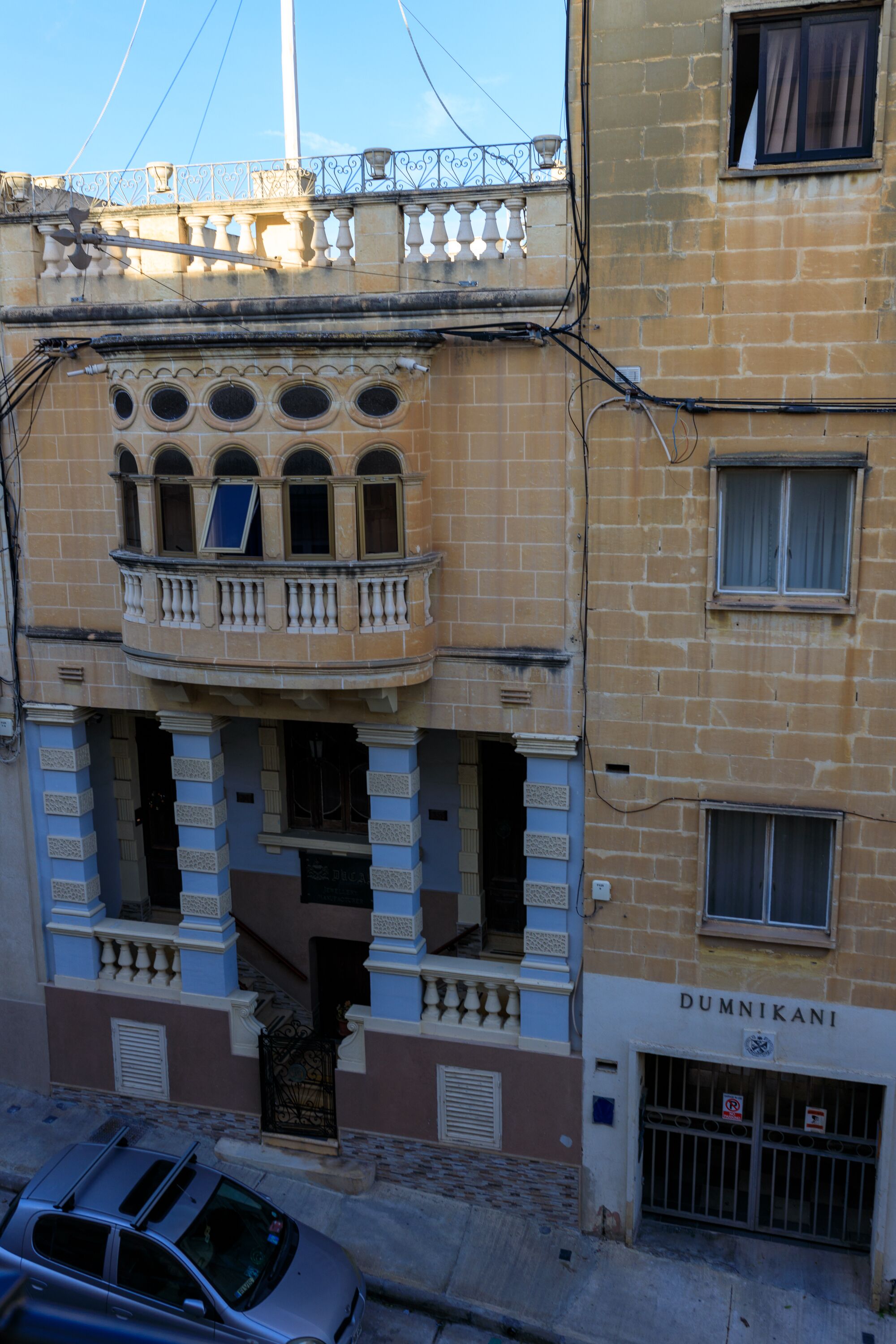A multi-story building with a balcony, a sign reading "DUMNIKANI," and a barred entrance.