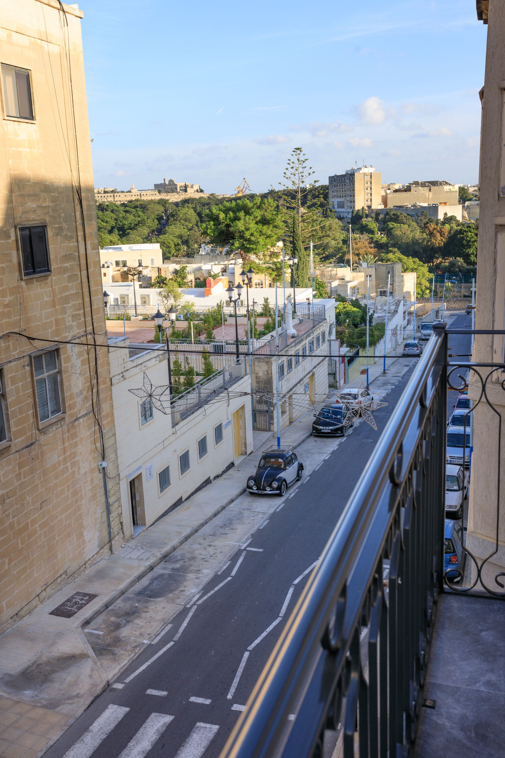 A street view from a balcony overlooking a cityscape with buildings, cars, and a clear sky.
