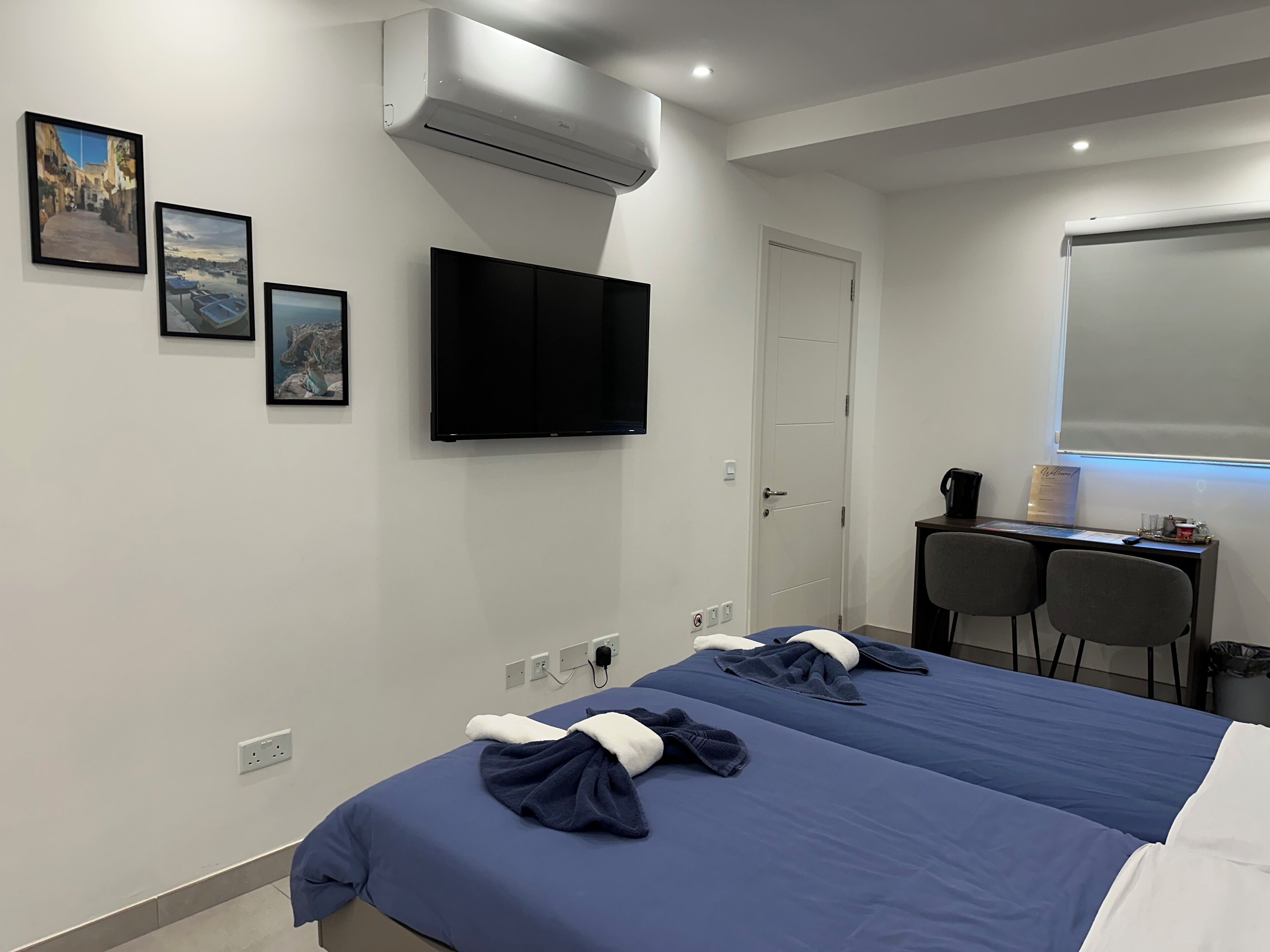 Habitación de hotel con cama, escritorio con dos sillas, televisor de pantalla plana y obras de arte en la pared.