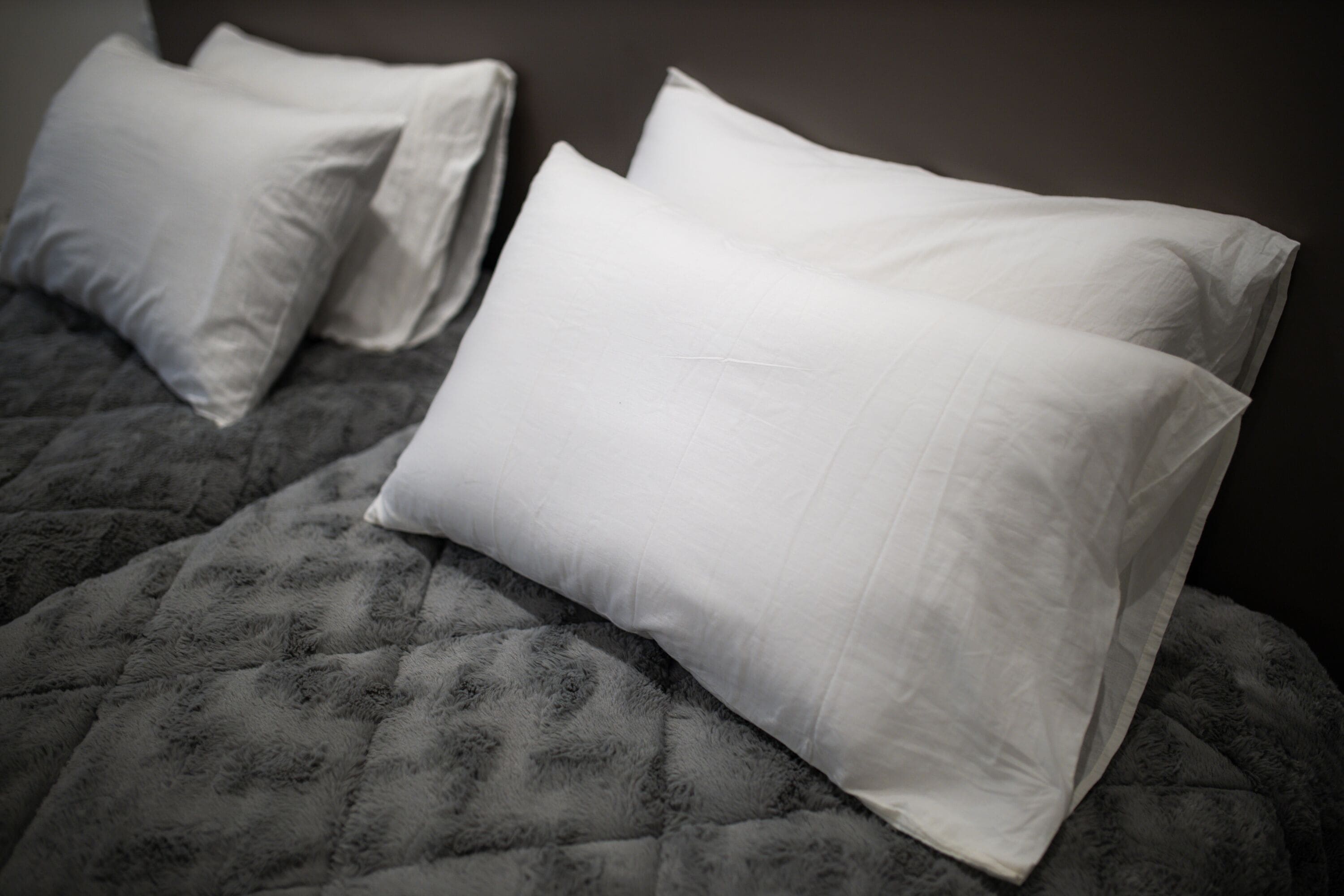 Una cama con cubrecolcha gris acolchado y dos almohadas blancas.
