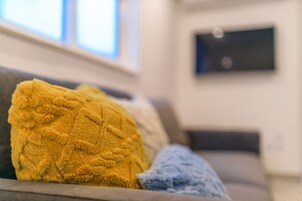 Un soggiorno con un divano, un cuscino giallo e uno blu, e un televisore a schermo piatto montato a parete.