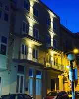 Un edificio de varios pisos con balcones, una farola y coches aparcados.