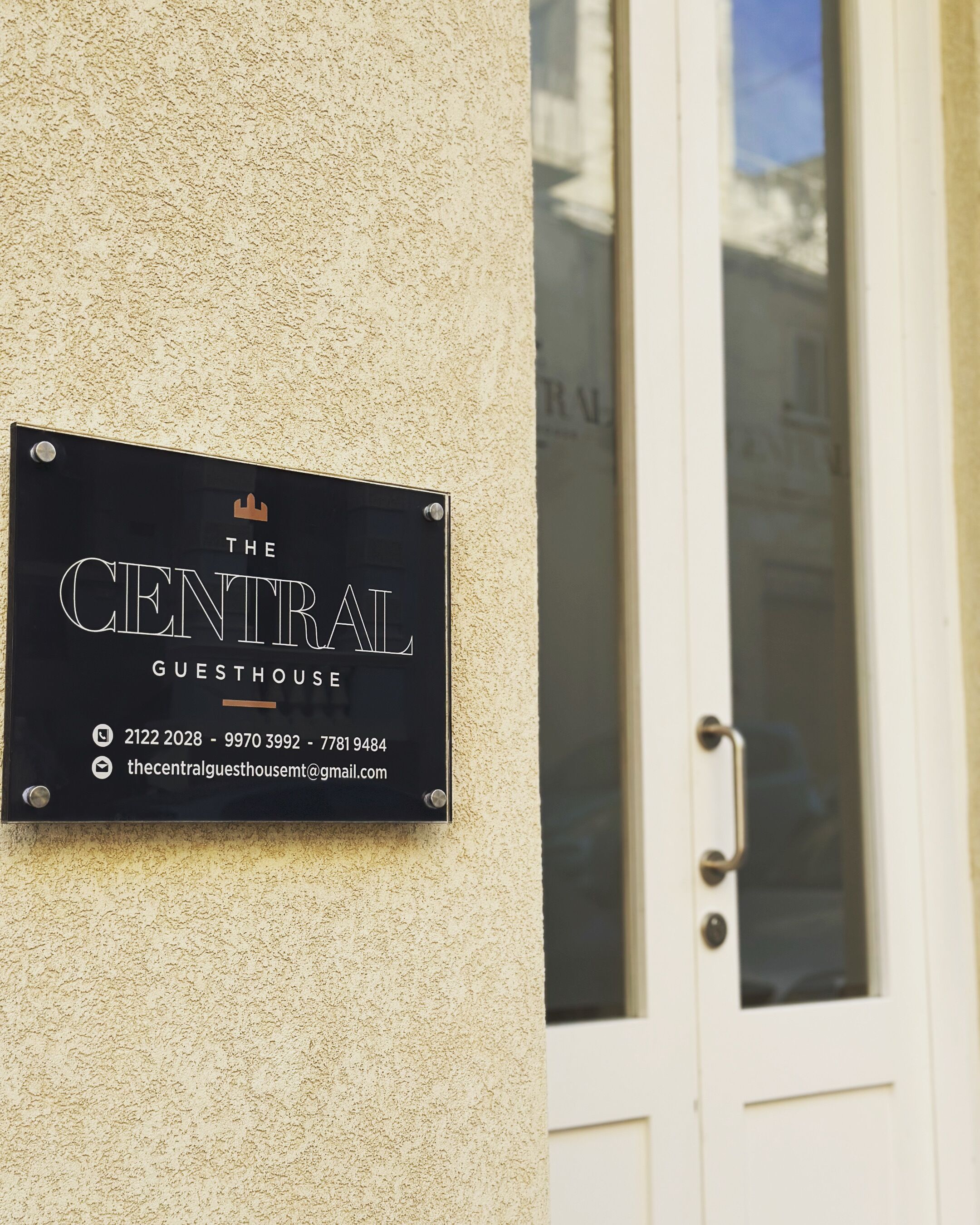 Segno nero su una parete strutturata con il testo 'The CENTRAL GUESTHOUSE' e informazioni di contatto.