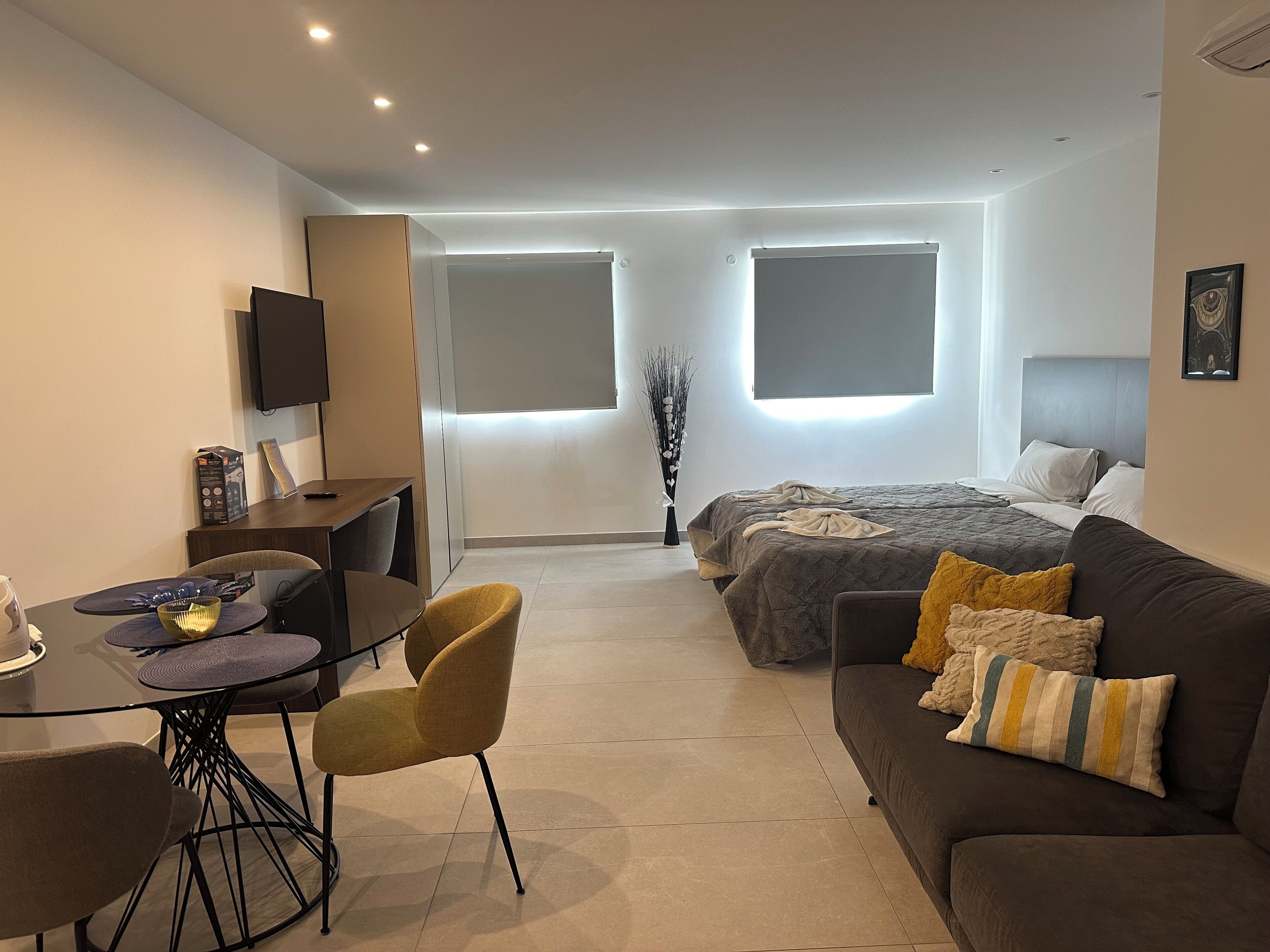 Ett modernt hotellrum med en säng, en soffa, ett matbord med stolar, en TV och ett stort fönster.