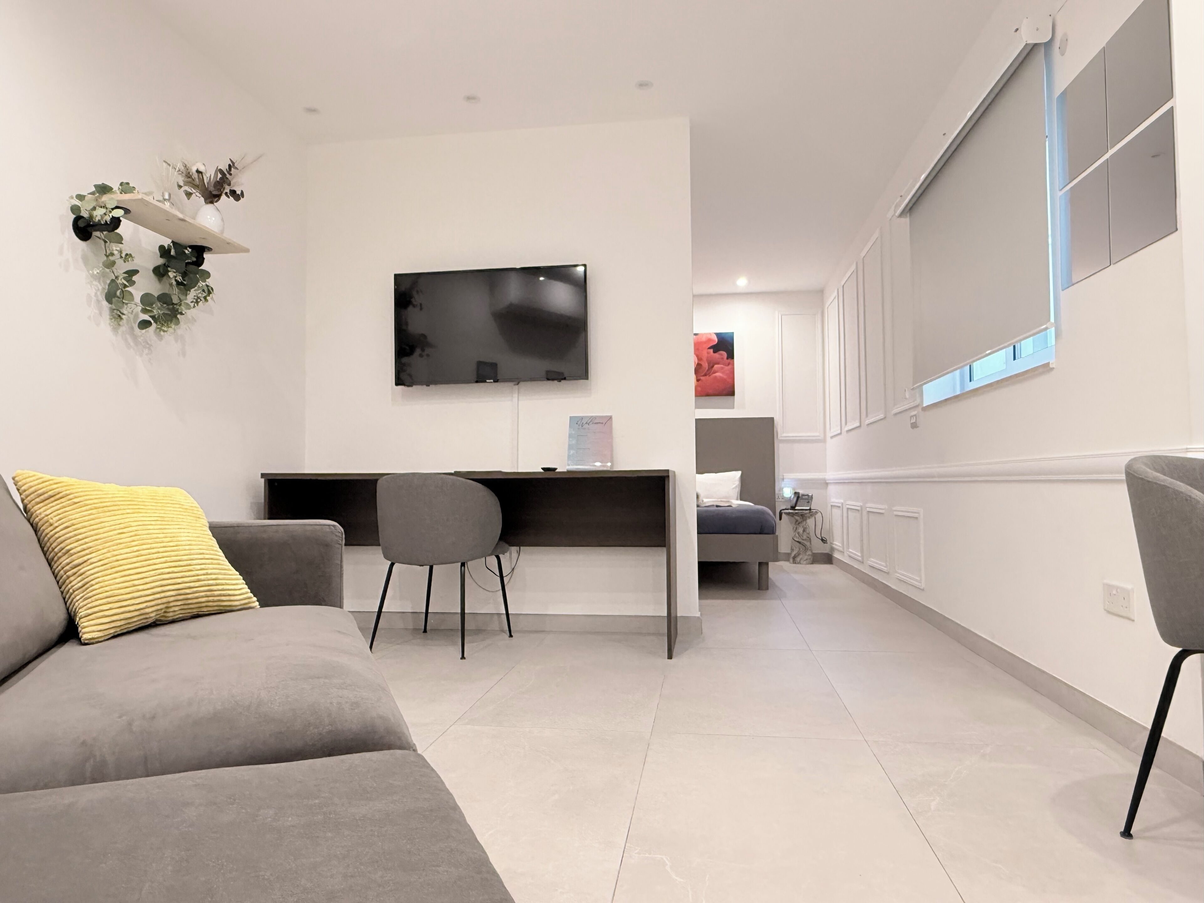 Una sala de estar moderna con un sofá gris, un escritorio pequeño y un televisor montado en la pared.