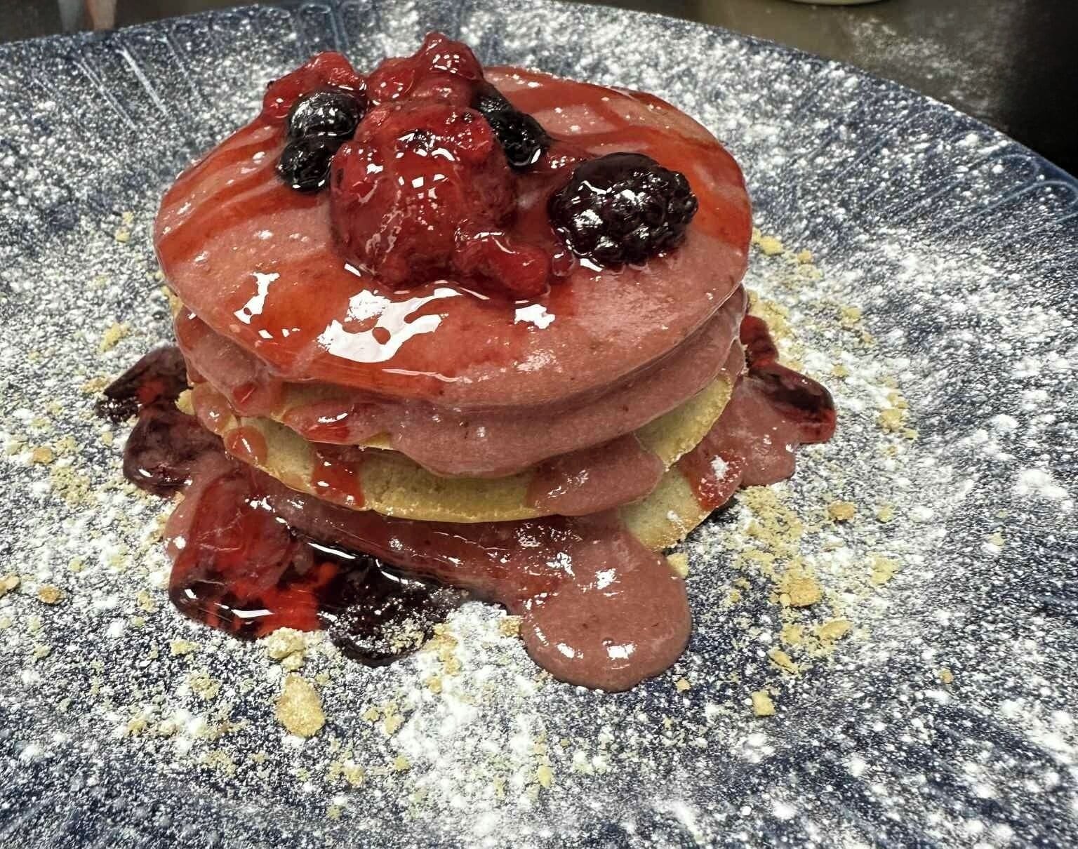 Una pila di pancake con sciroppo e frutti di bosco su un piatto screziato.