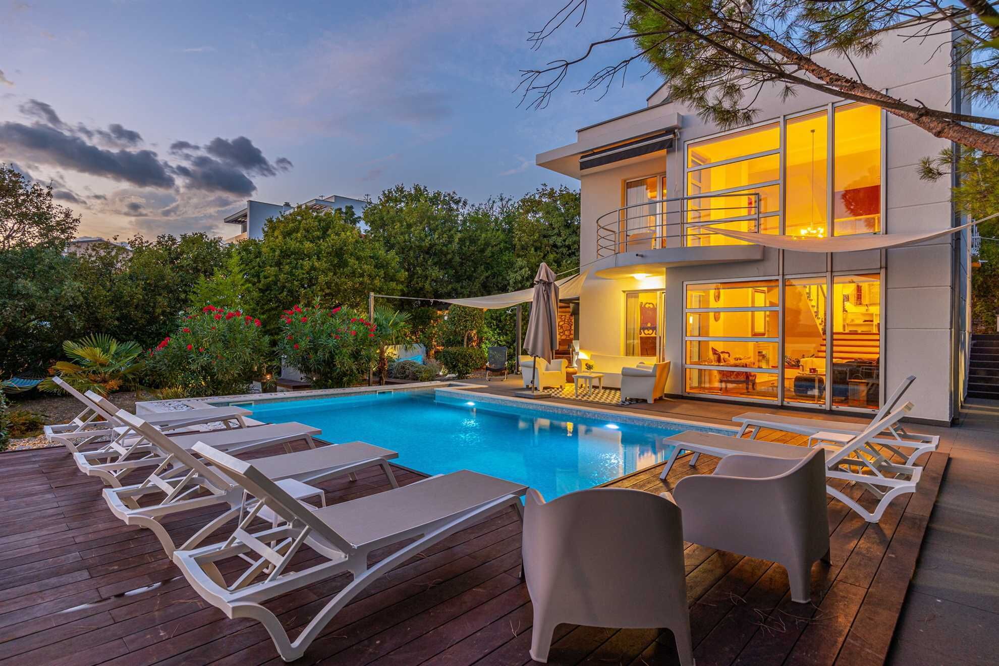 A modern two-story house with a swimming pool, deck chairs, and a covered patio area.