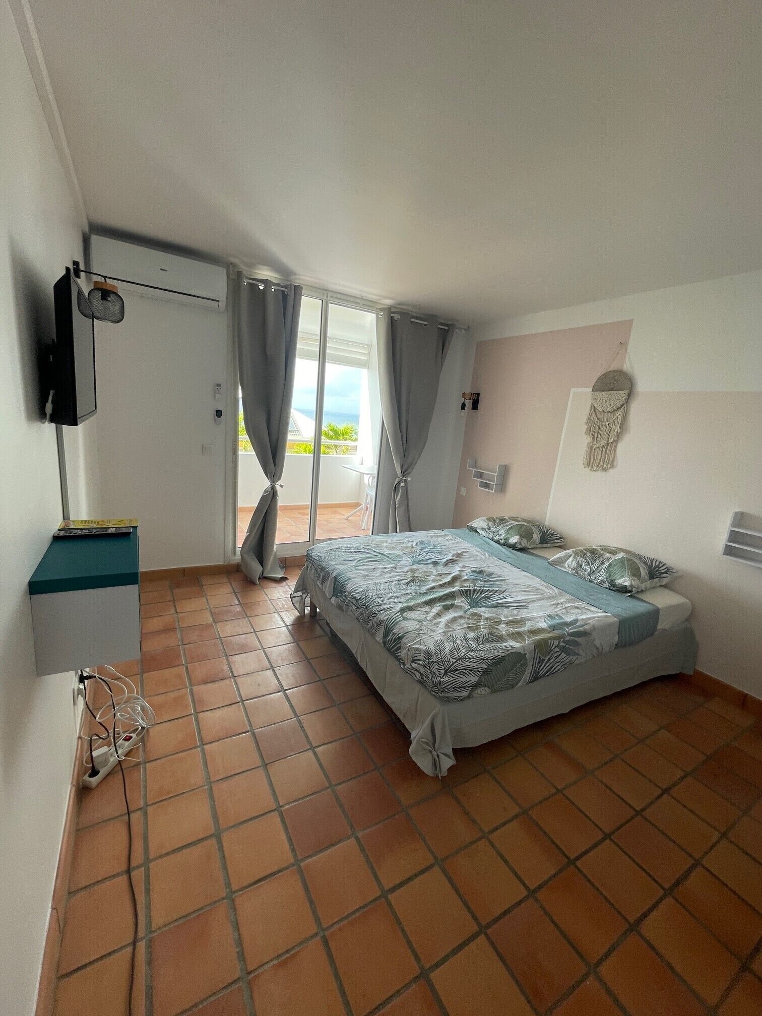 A bedroom with a bed, a TV, a desk, and a balcony with curtains.
