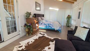 Un vaste salon agrémenté d’un tapis en peau de vache, de canapés sombres, d’un ventilateur de plafond et d’un lit recouvert d’une couvre-lit à motifs bleus et blancs.