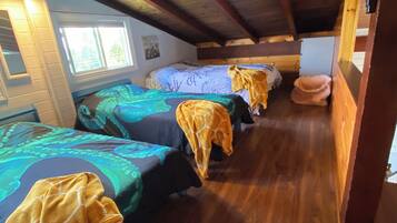 Fileira de beliches de madeira com roupa de cama colorida, uma janela e teto de madeira.