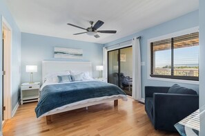 A modern bedroom with a bed, bedside tables, a ceiling fan, a window with blinds, and a view of the outdoors.