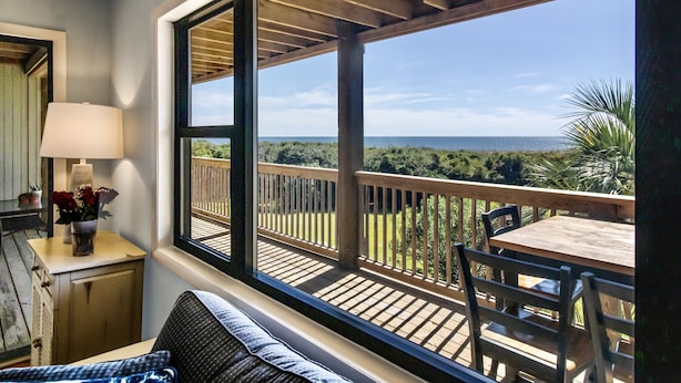 Un balcon doté d’une terrasse en bois, d’une table avec des chaises et d’une vue sur l’océan.