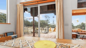 A room with a large sliding glass door leading to an outdoor area. Inside, there is a wooden table with a woven placemat and a yellow woven mat.