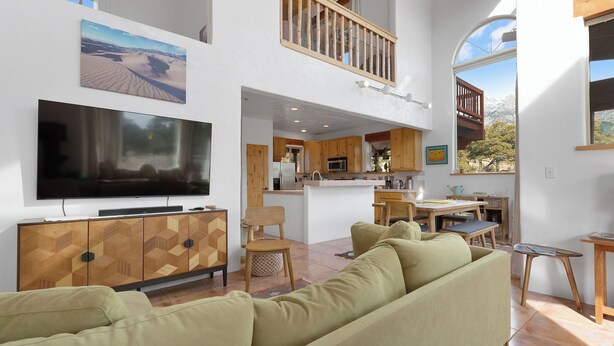 A spacious living area with a large flat-screen TV, a wooden cabinet, a beige sofa, and a dining area with wooden furniture.