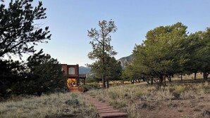 A rustic wooden cabin with a stone pathway leading to it, surrounded by trees and a mountainous backdrop.