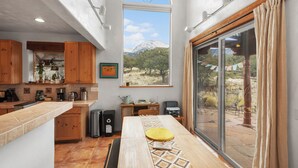 A modern kitchen with wooden cabinets, a large island, and a view of a mountainous landscape through a large window.