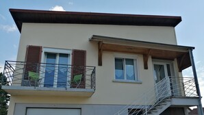 Um edifício de dois andares com fachada branca, uma varanda com grades de metal e uma escadaria que leva ao andar superior.