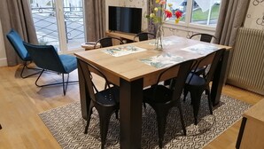Uma área de refeições com uma mesa de madeira, cadeiras pretas e um vaso com flores.