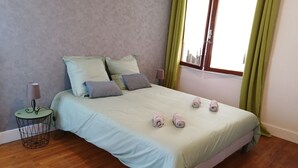 Cama bem arrumada com roupa de cama e almofadas azul claro, um abajur e toalhas dobradas sobre a cama.