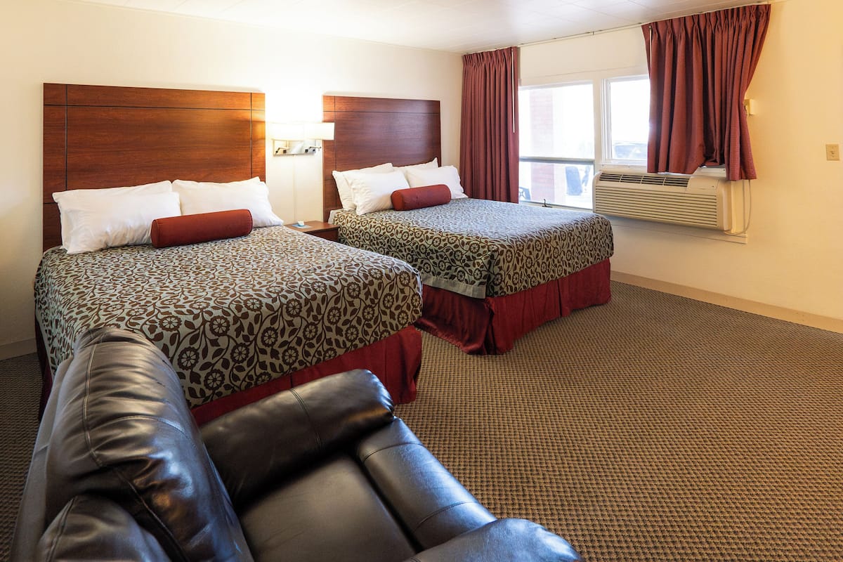 A hotel room with two beds, a leather couch, and an air conditioning unit.