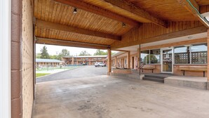 A covered parking area with a concrete floor, wooden beams, and a view of a building with multiple windows and a brick facade. - Hot Springs Hills Inn (Hot Springs)