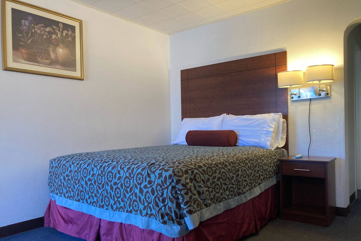 A hotel room with a bed, a nightstand, a lamp, and a framed picture on the wall.
