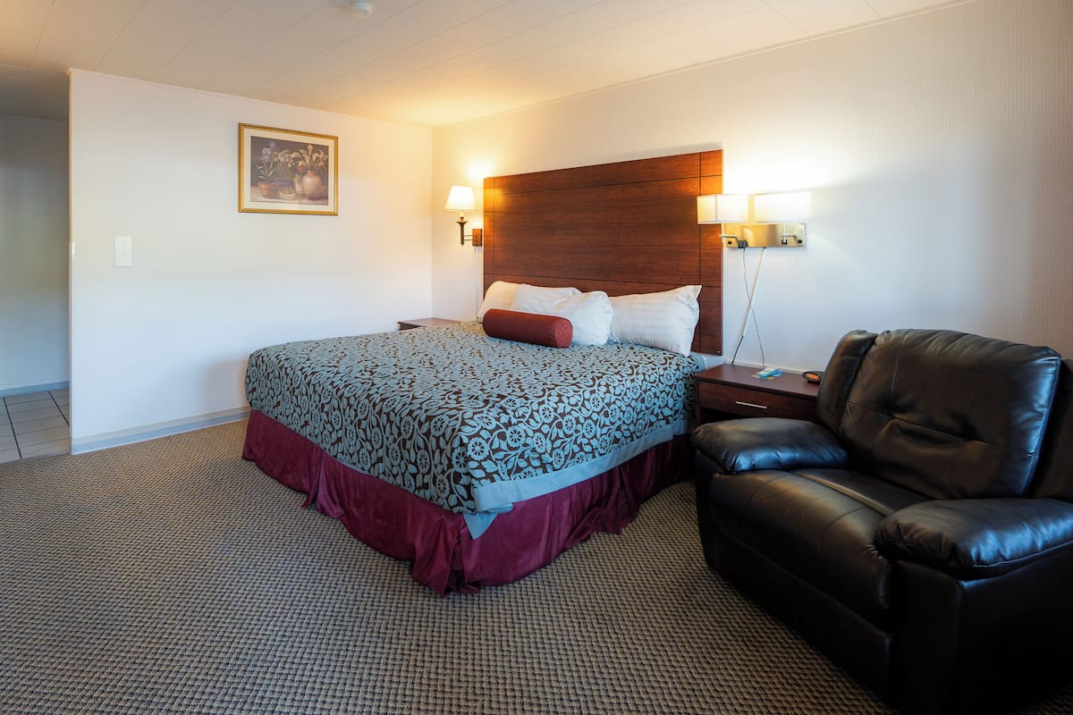 A hotel room with a large bed, a leather armchair, and a nightstand with a lamp.